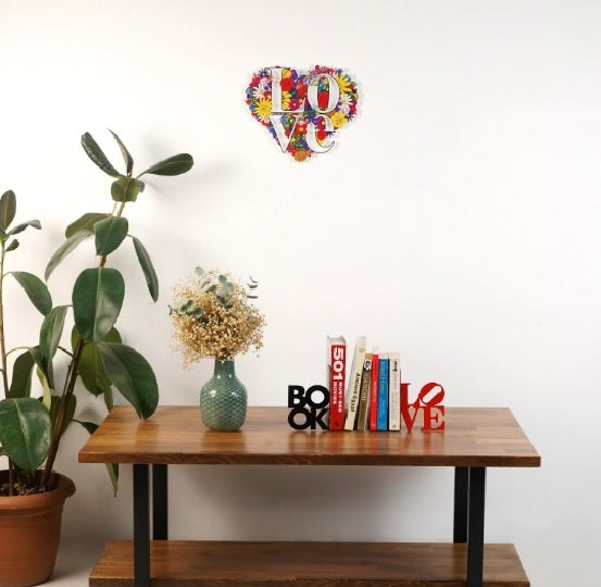 BOOK ve LOVE yazılı metal kitap tutucu, ahşap sehpanın üzerinde, arkada duvarda çiçek desenli LOVE kalbi