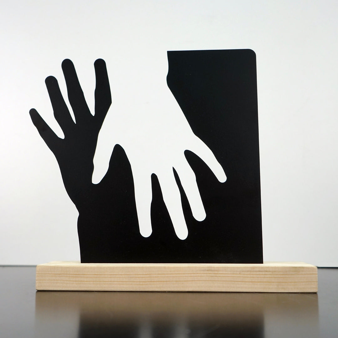 Siyah metal çift tutuşan elleri masa dekoru, açık renk masif ahşap altlıkta, önden görünüm