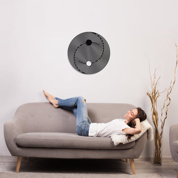 Siyah Yin Yang dekoratif metal duvar tablosu, gri kanepede uzanan kişinin üstündeki duvarda